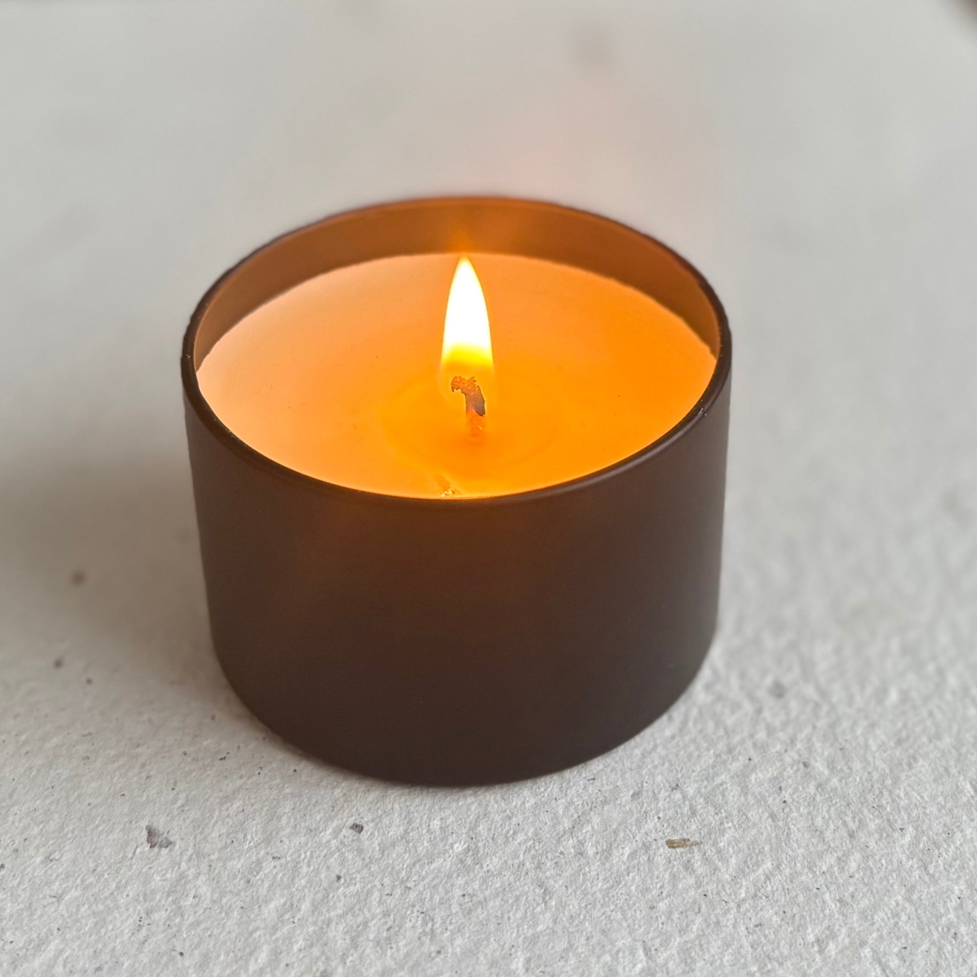 Black organic candle with a flame, on a white surface.