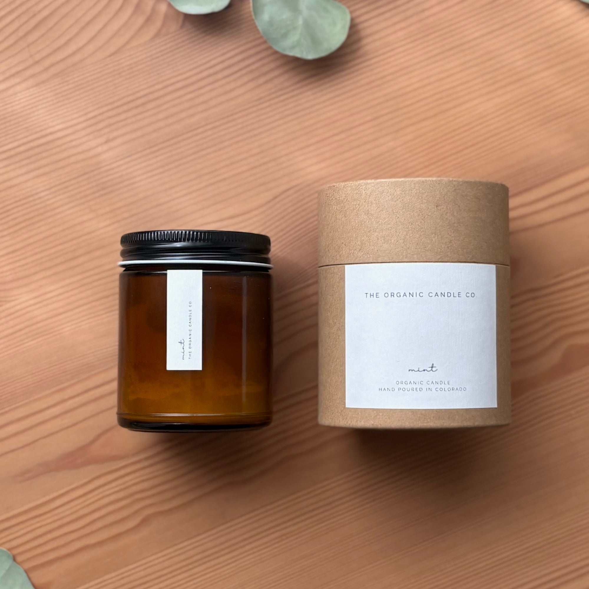 Amber jar organic candle with black lid and its packaging on a wooden surface