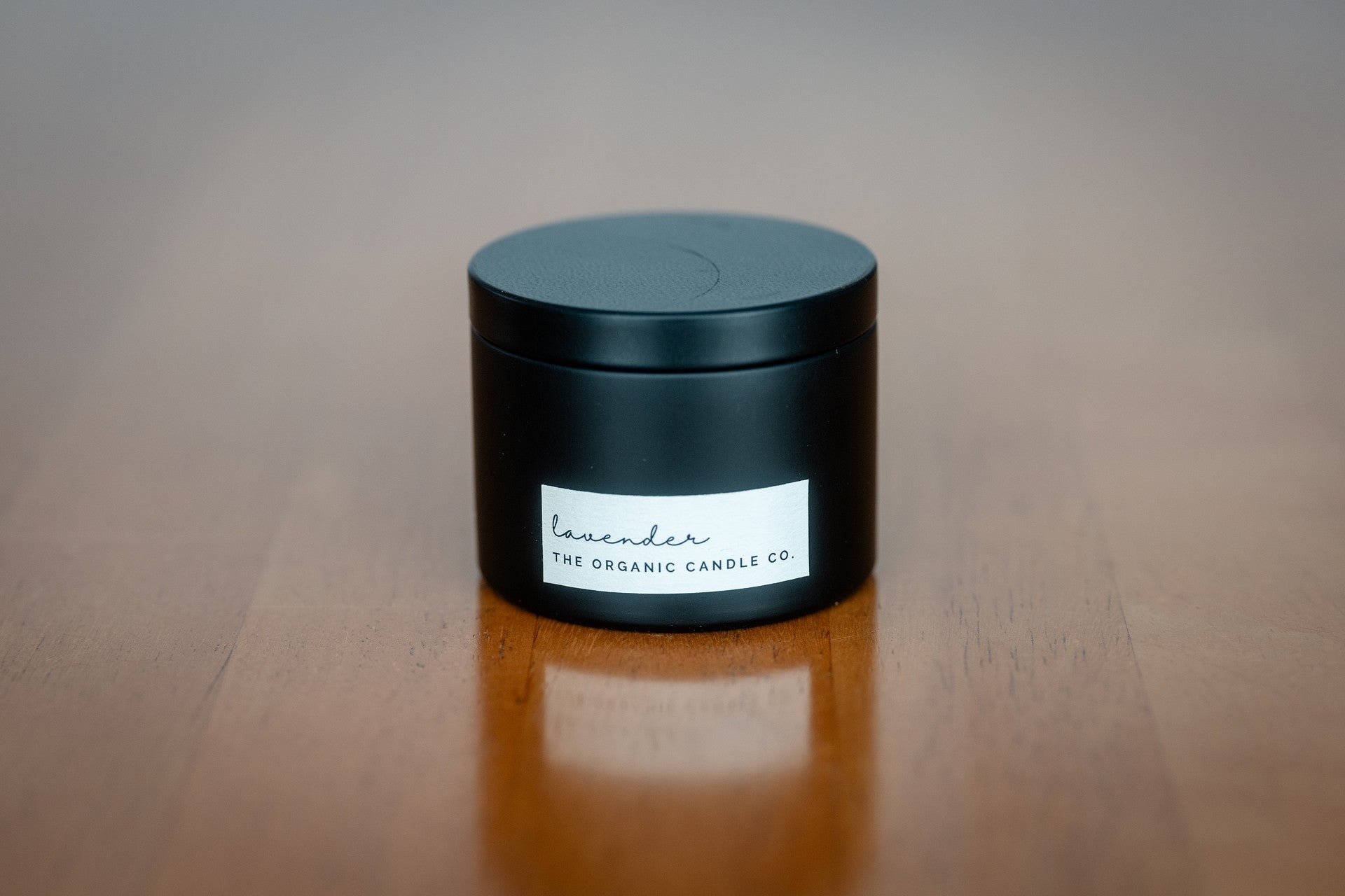 Organic candle in a black container with a white label on a wooden surface