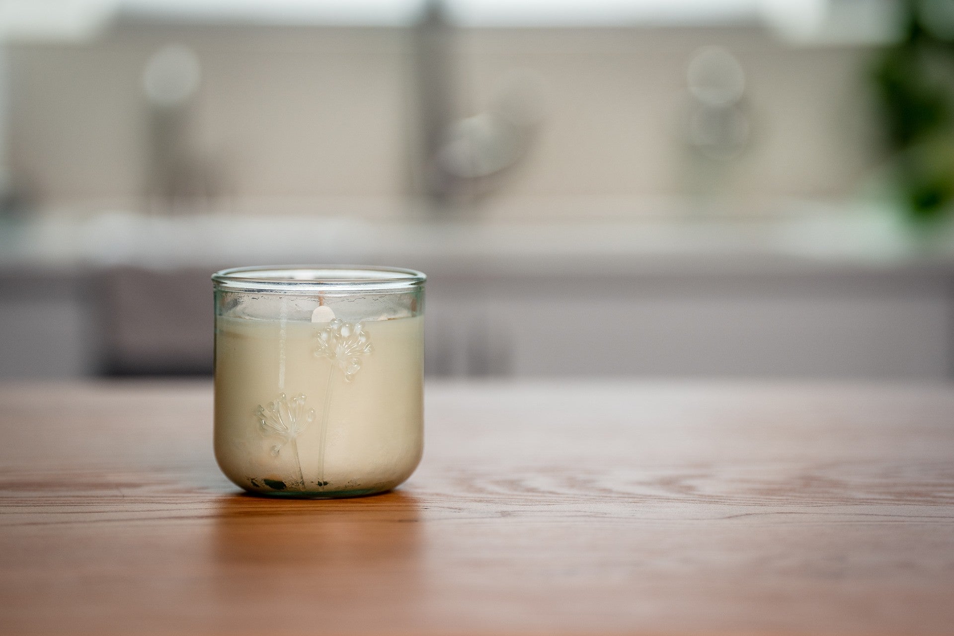 Clear recycled glass jar with a white organic candle on a wooden surface in a blurred kitchen setting