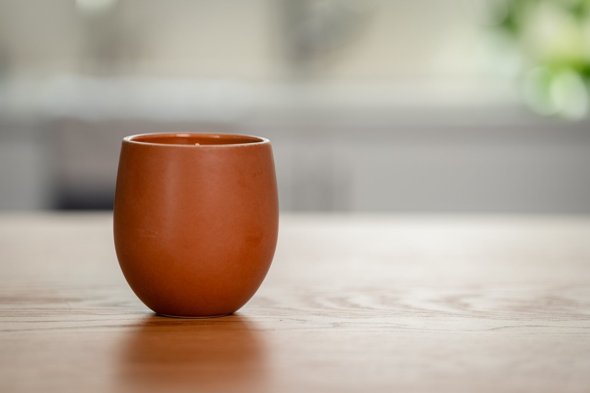 Terracotta-colored ceramic organic candle on a wooden surface with a blurred background