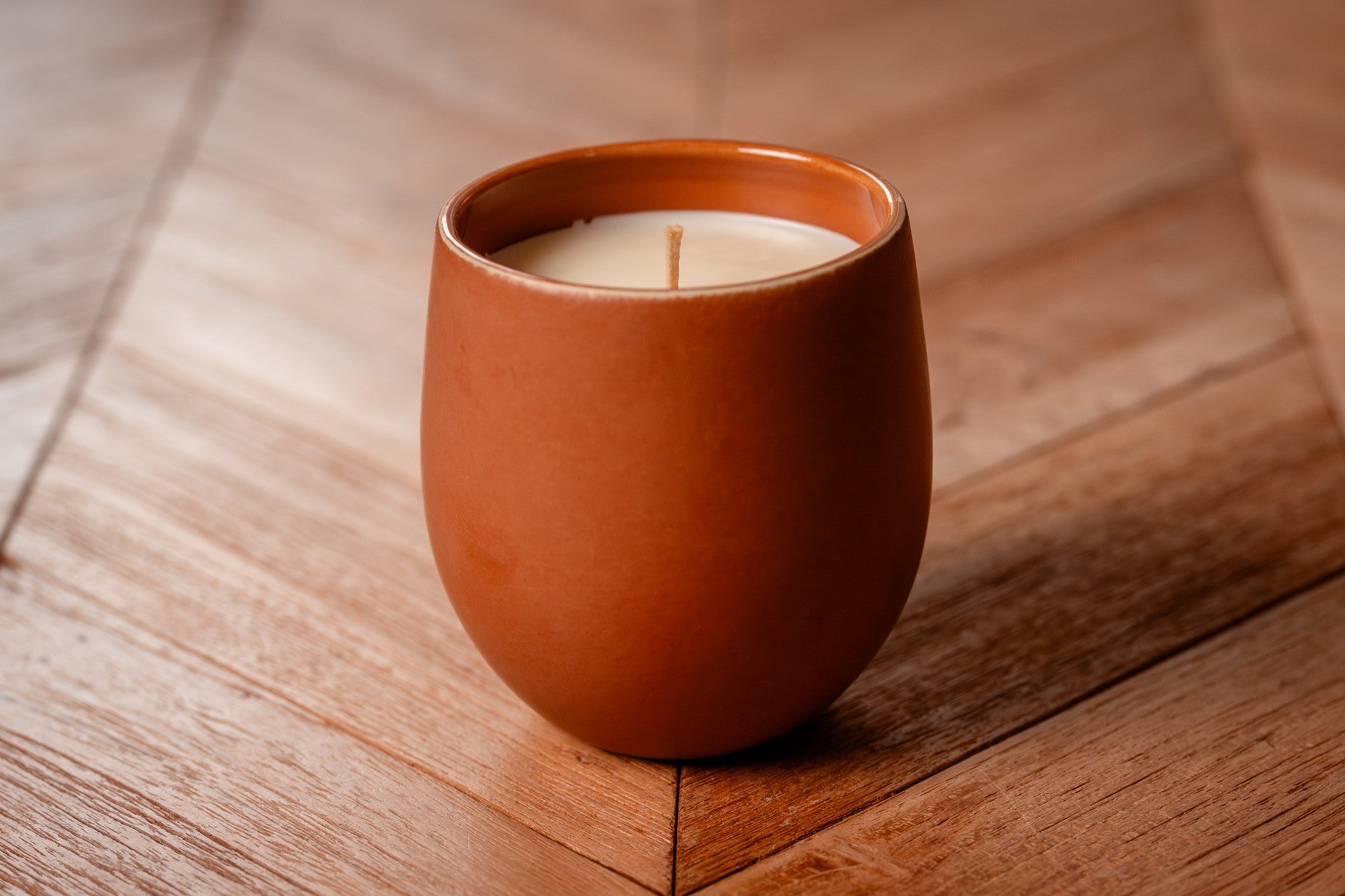 Ceramic organic candle in a terra cotta color on a wooden surface