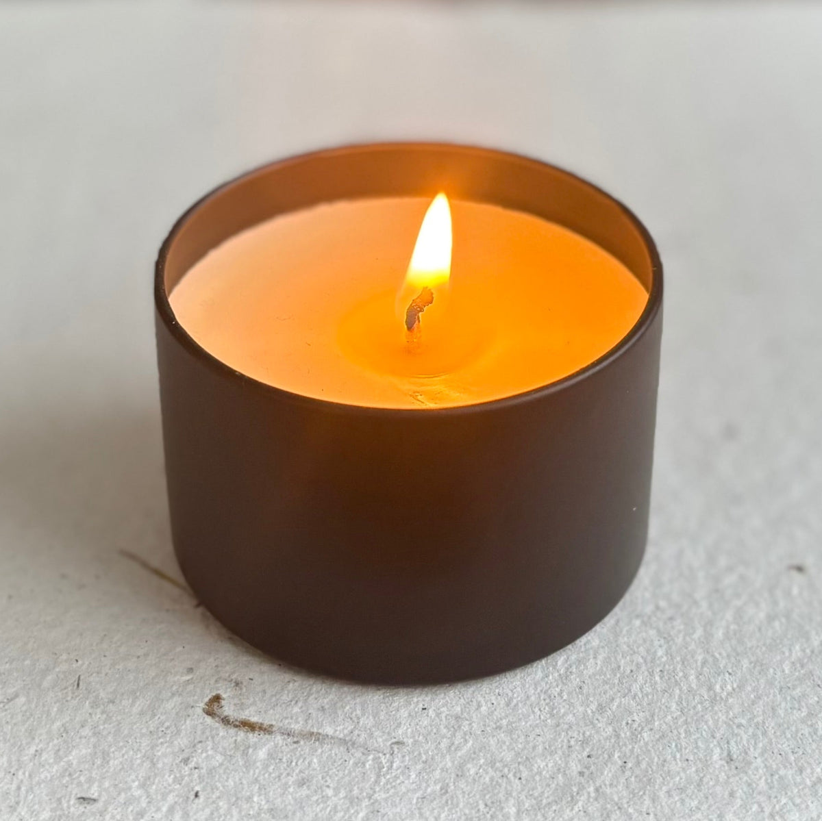 Small lit organic candle in a black holder on a light gray surface