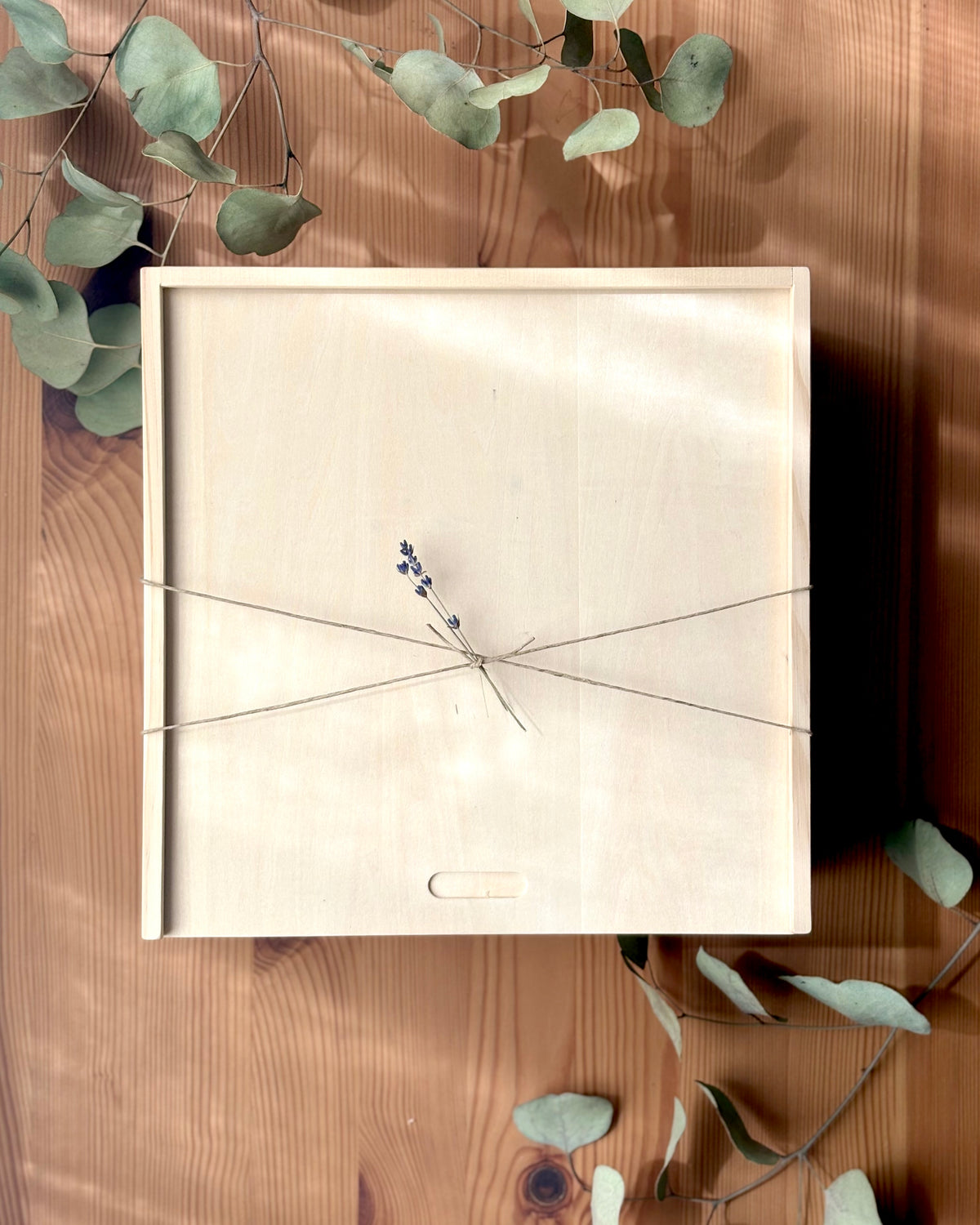 Wooden box with string closure on a wooden surface with eucalyptus leaves.