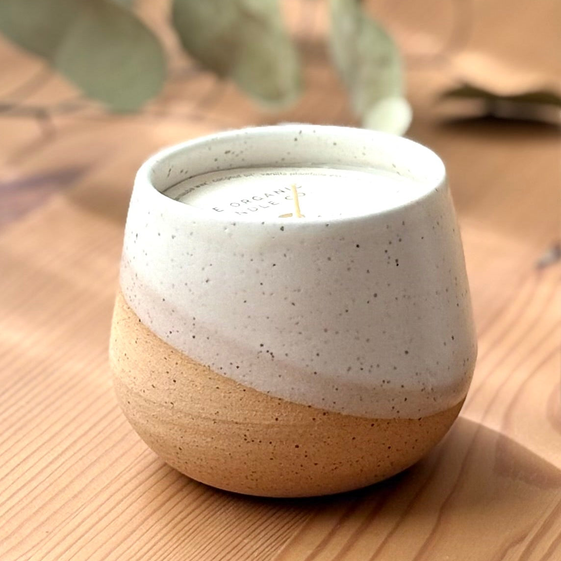 Ceramic organic candle on a wooden surface with eucalyptus leaves.