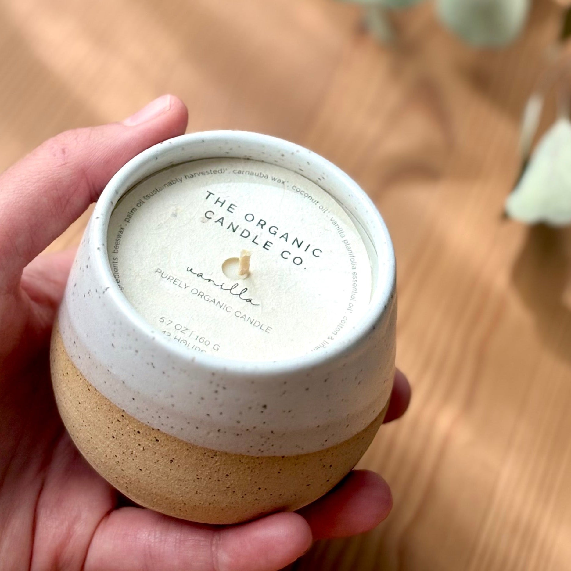 Hand holding a speckled ceramic organic candle with &