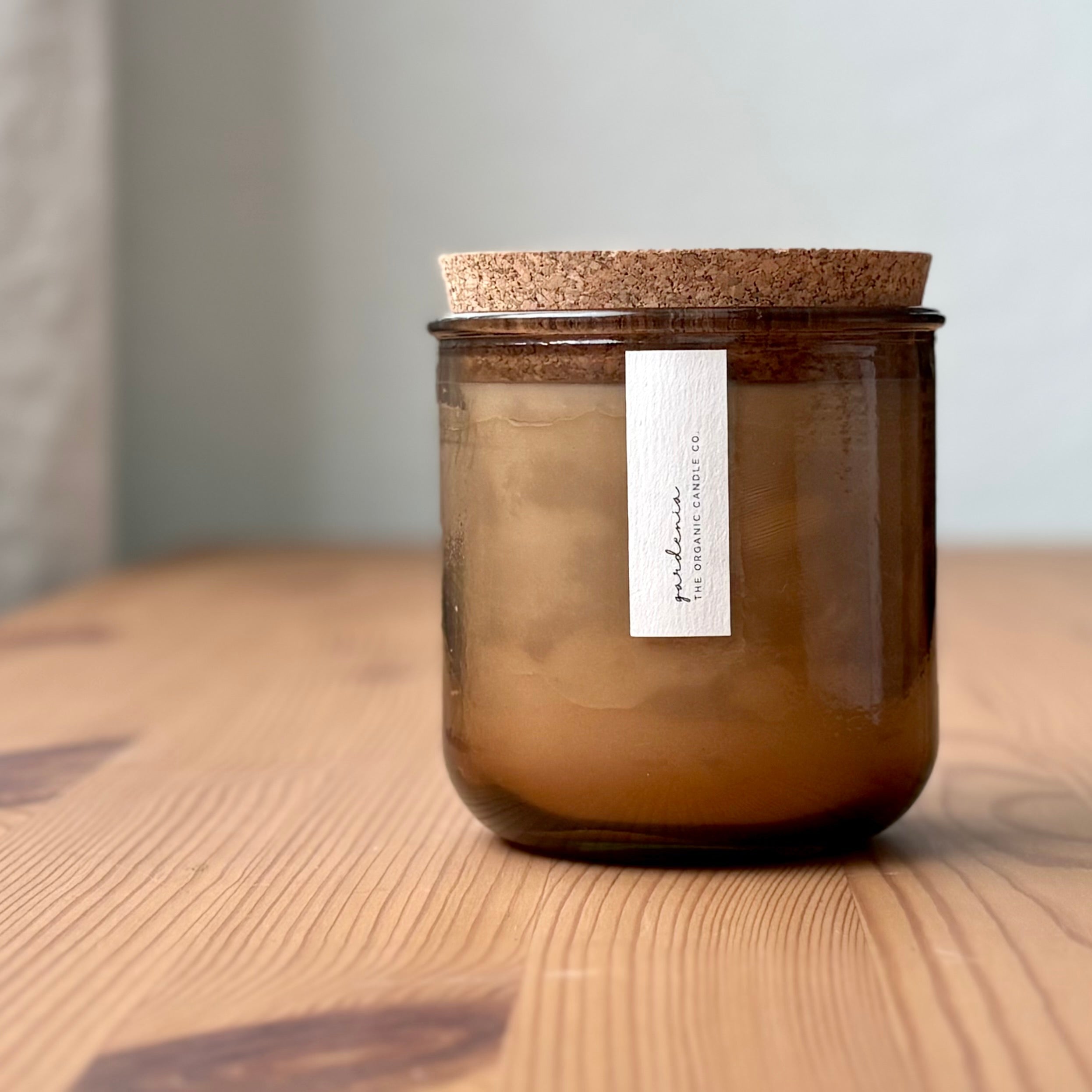Organic candle in rose recycled glass jar on a wooden background, with a cork top. A label reads "gardenia; The Organic Candle Co."