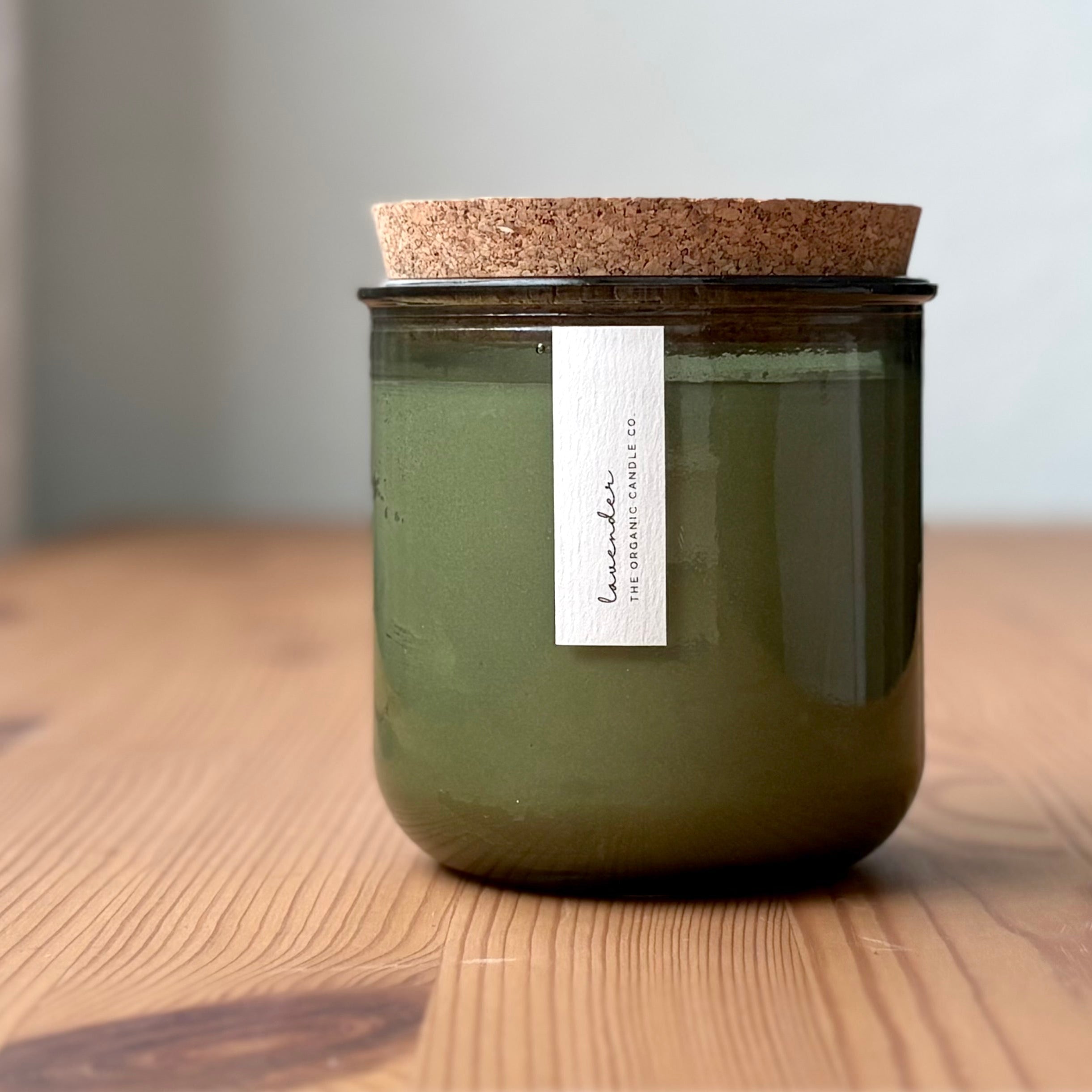 Organic candle in green recycled glass jar on a wooden background. A label reads "lavender; The Organic Candle Co."