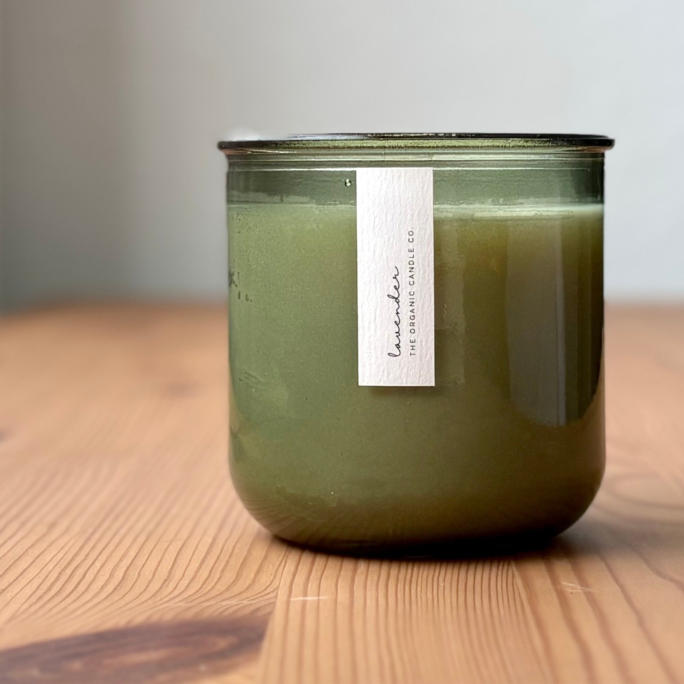 Organic candle in green recycled glass jar on a wooden background. A label reads "lavender; The Organic Candle Co."