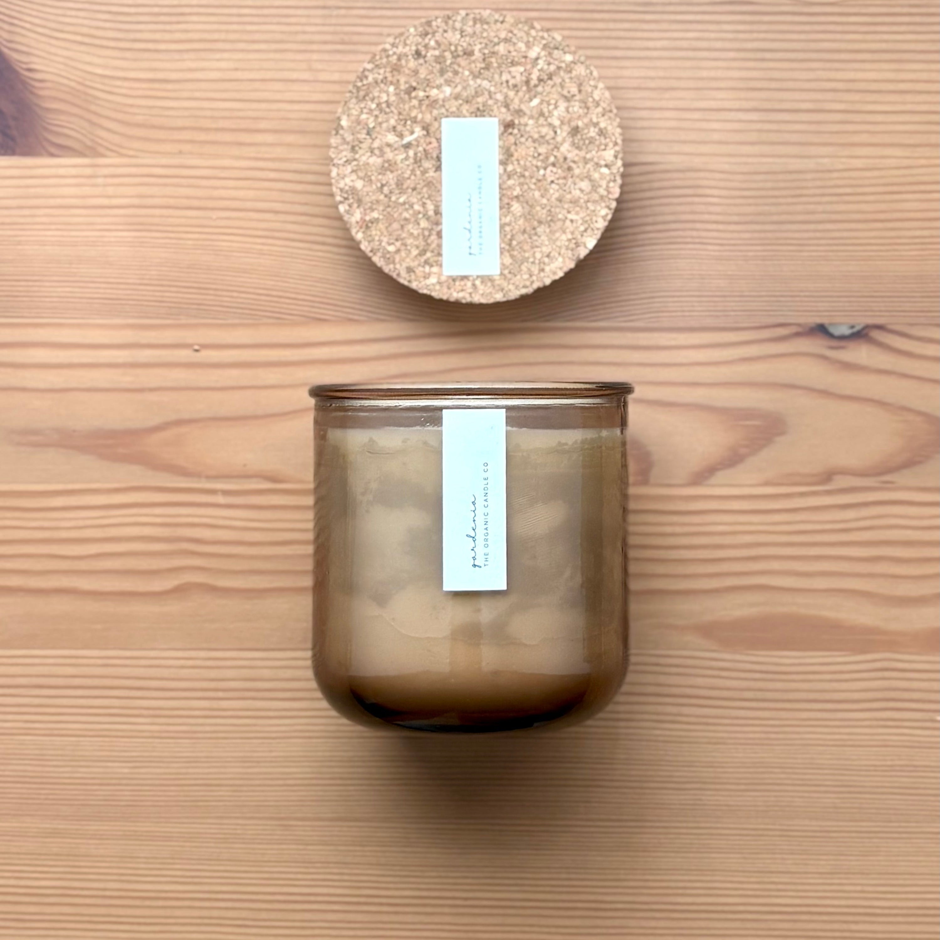 Organic candle in rose recycled glass jar on a wooden background, with a cork top. A label reads "gardenia; The Organic Candle Co."