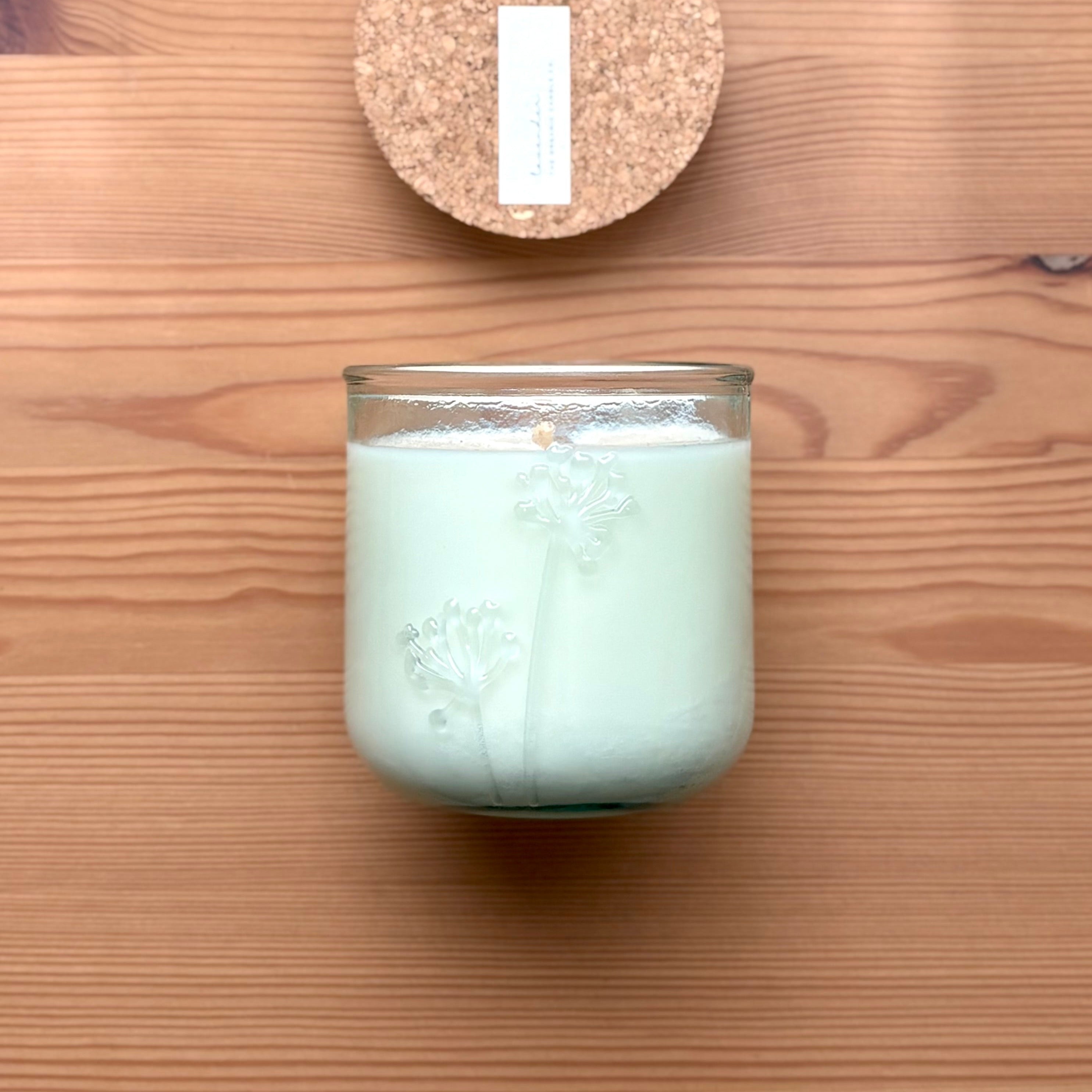 Organic candle in a recycled glass floral jar on a wooden surface