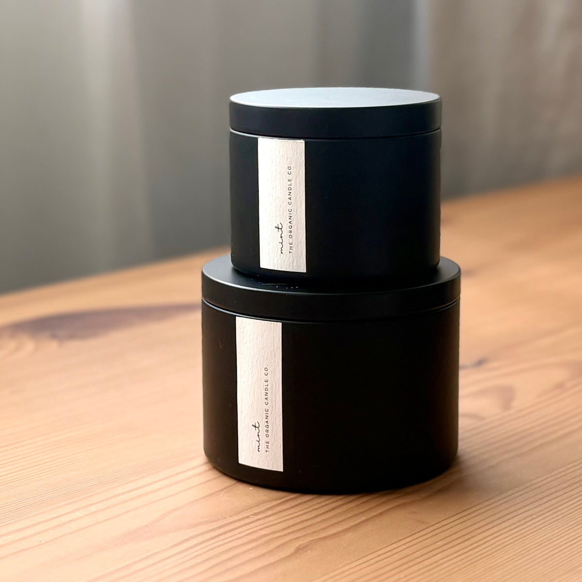 Two organic candles in black metal containers with labels on a wooden surface