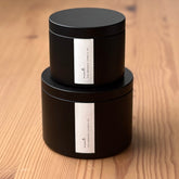 Two black organic candles with labels on a wooden surface