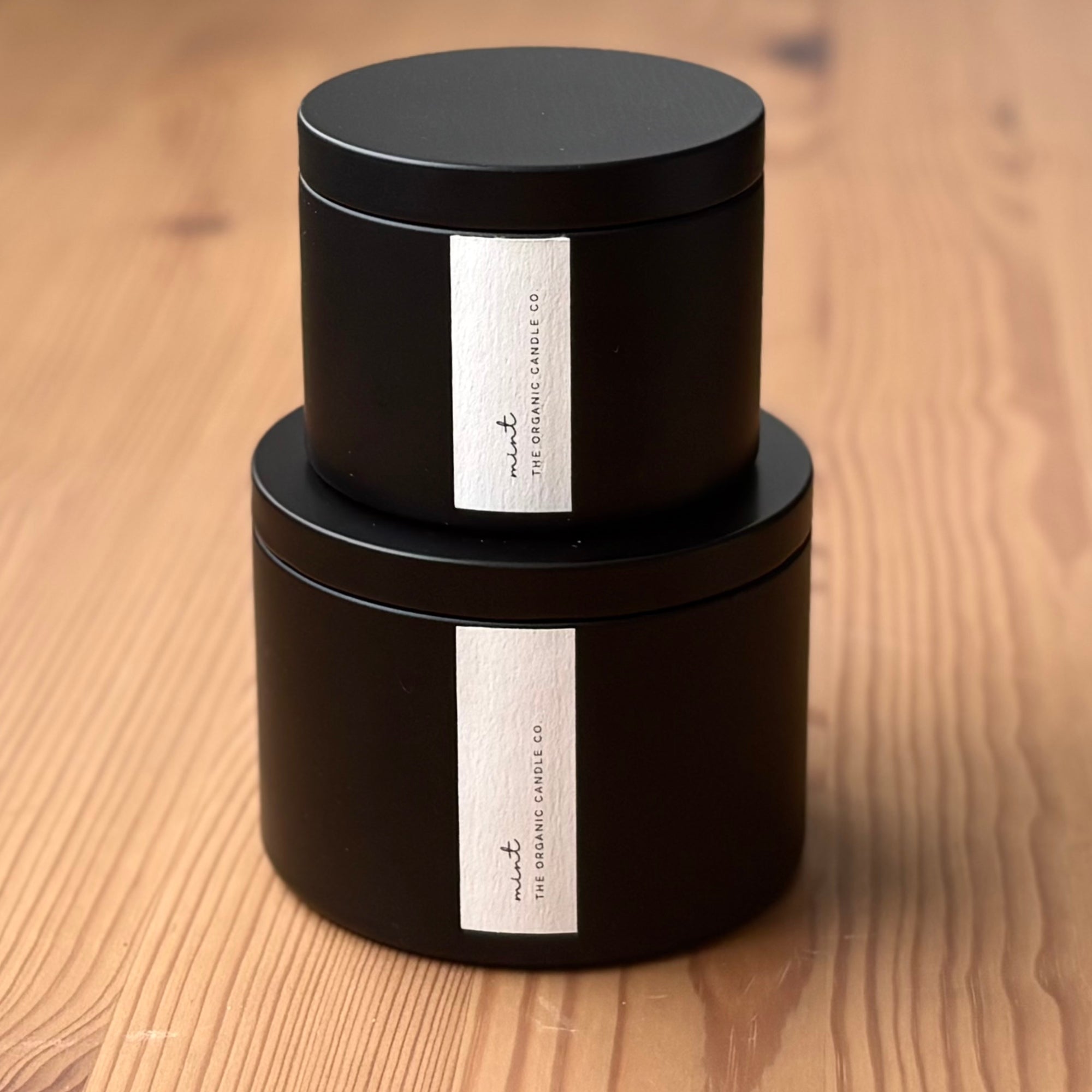 Two black organic candles with labels on a wooden surface