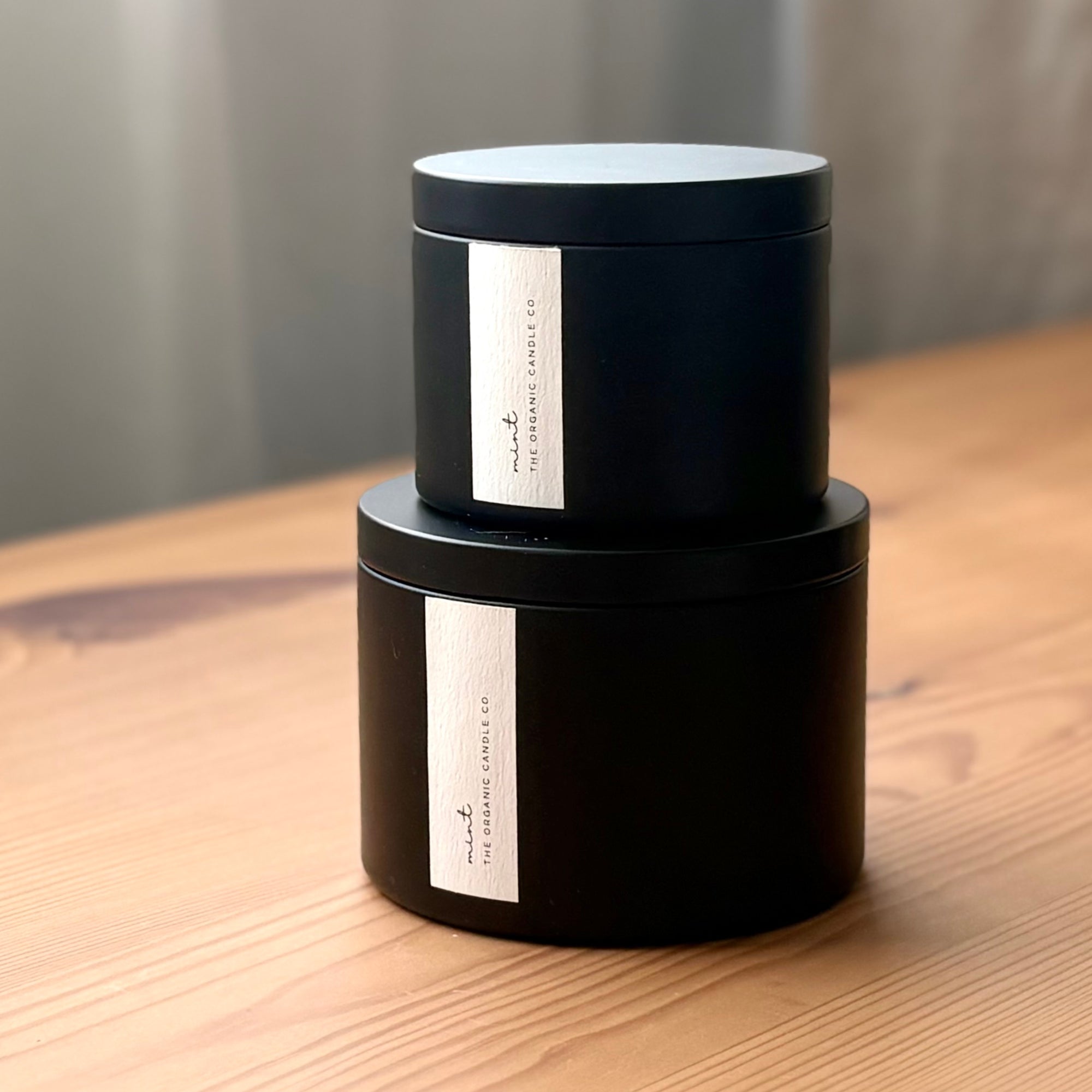 Two black organic candle jars with a white label on a wooden surface