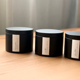 Three black organic candles with labels on a wooden surface