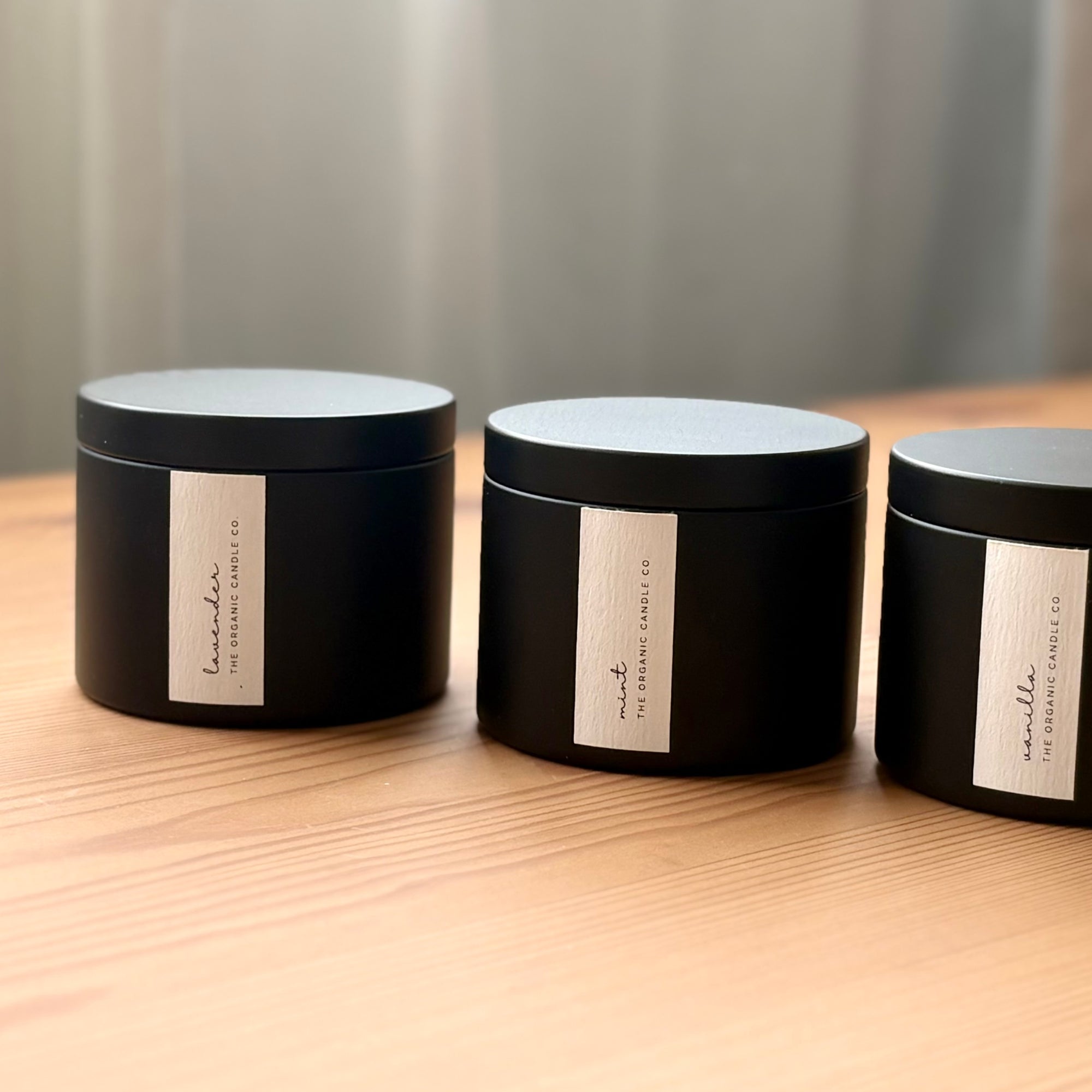 Three black organic candles with labels on a wooden surface