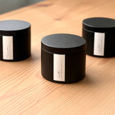 Three black organic candles with labels on a wooden surface