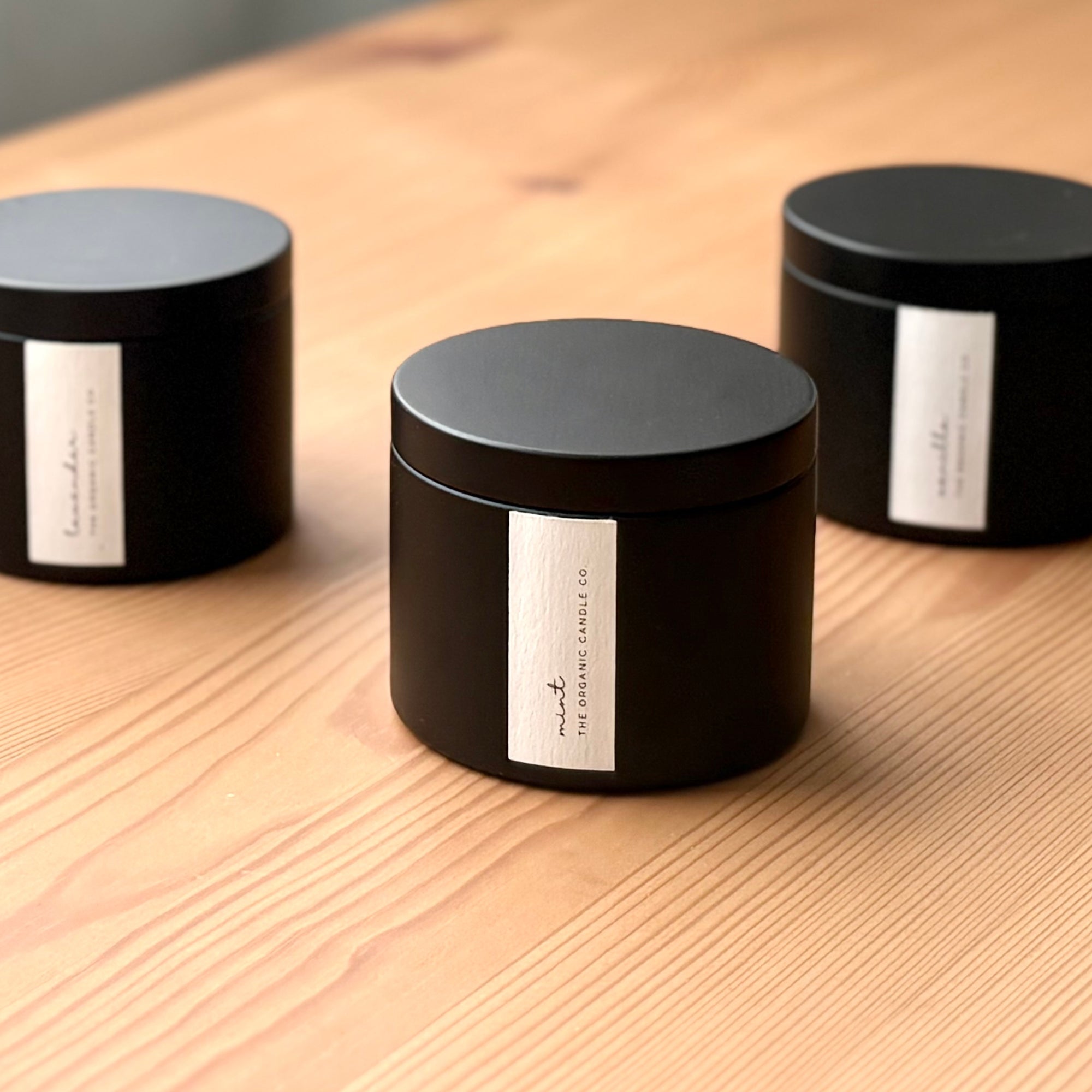 Three black organic candles with labels on a wooden surface
