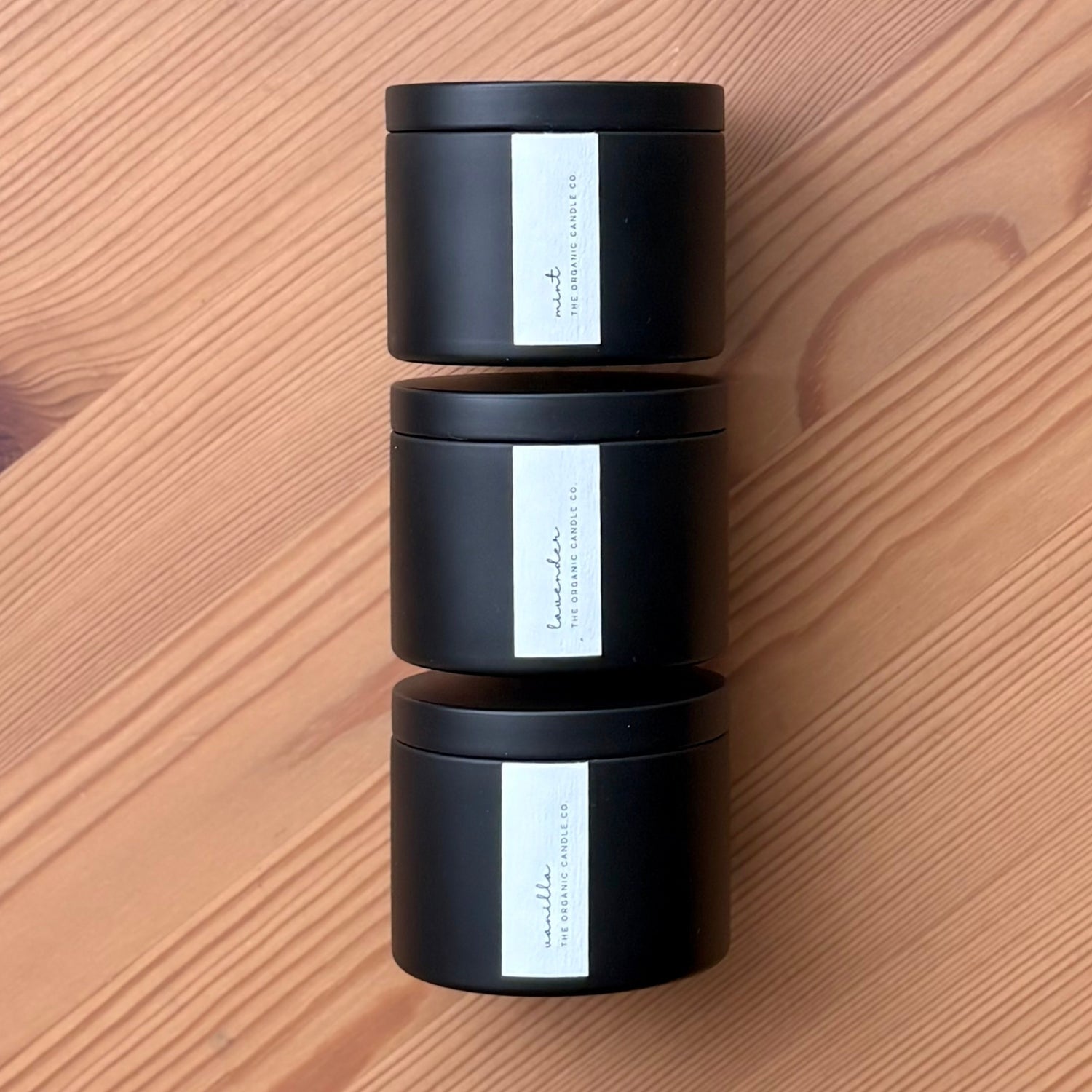 Three black organic candles with white labels stacked on a wooden surface