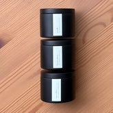 Three black organic candles with white labels stacked on a wooden surface