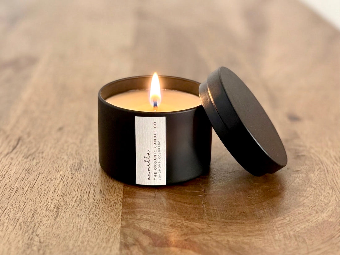 Organic candle in a black container with a lit wick on a wooden surface