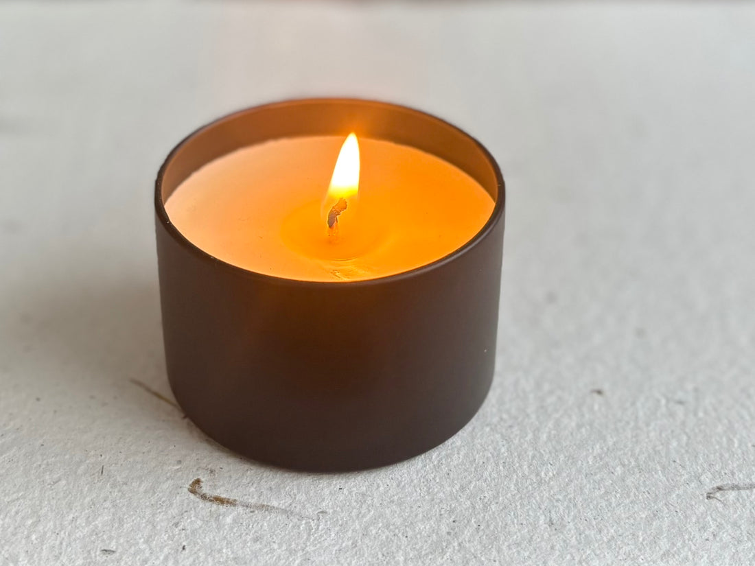 Small lit organic candle in a black holder on a light gray surface