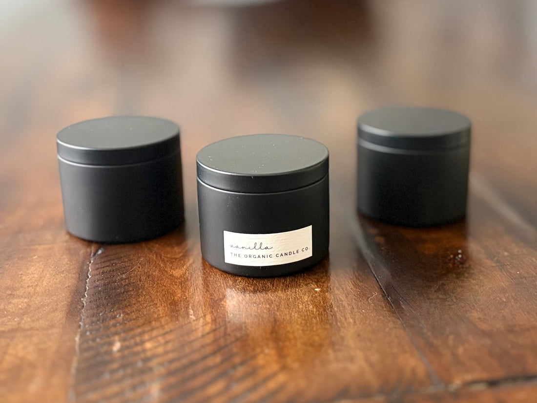 Three black organic candle containers on a wooden surface with a blurred background