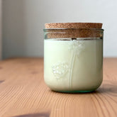 Organic candle in a recycled glass floral jar with a cork, on a wooden surface.