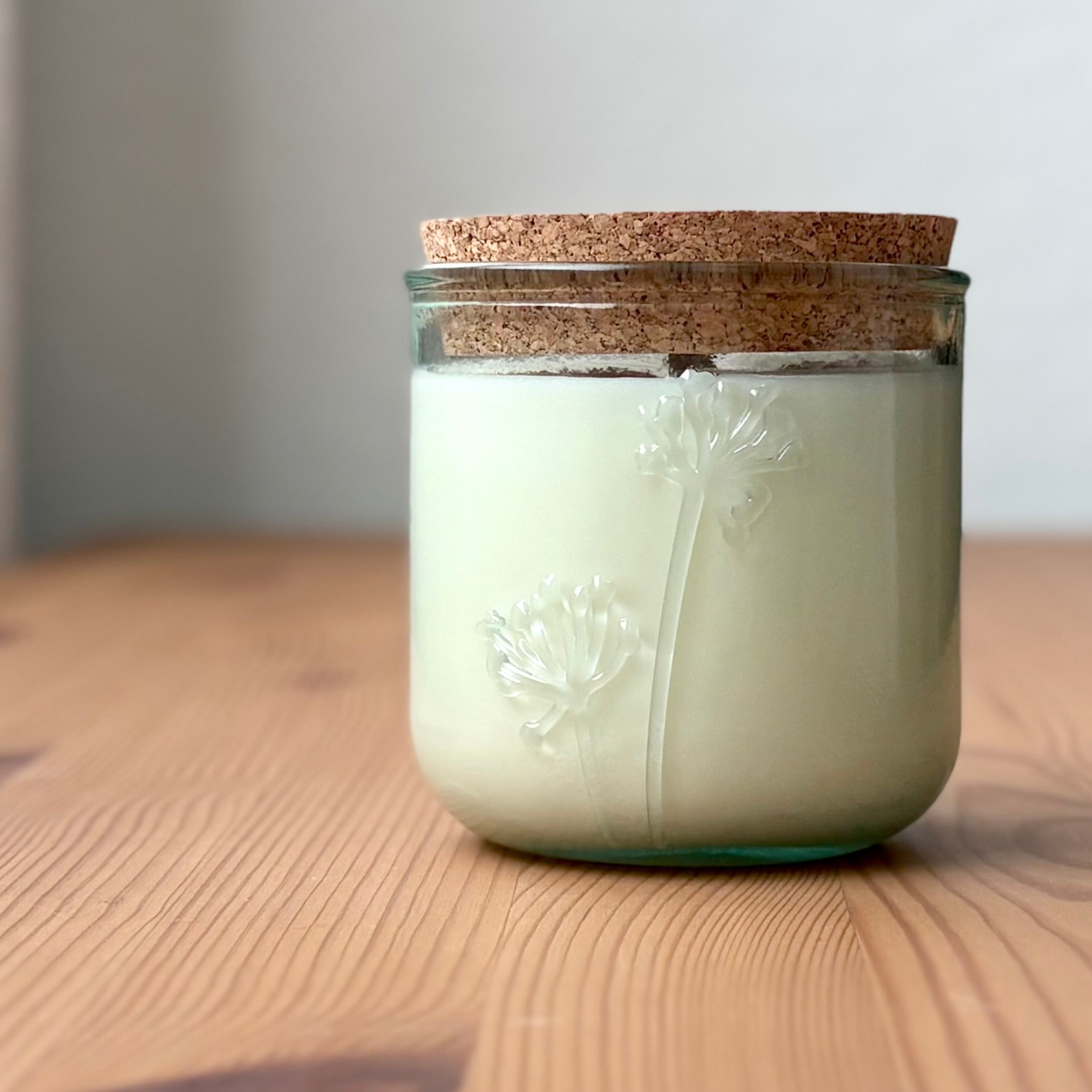 Organic candle in a recycled glass floral jar with a cork, on a wooden surface.