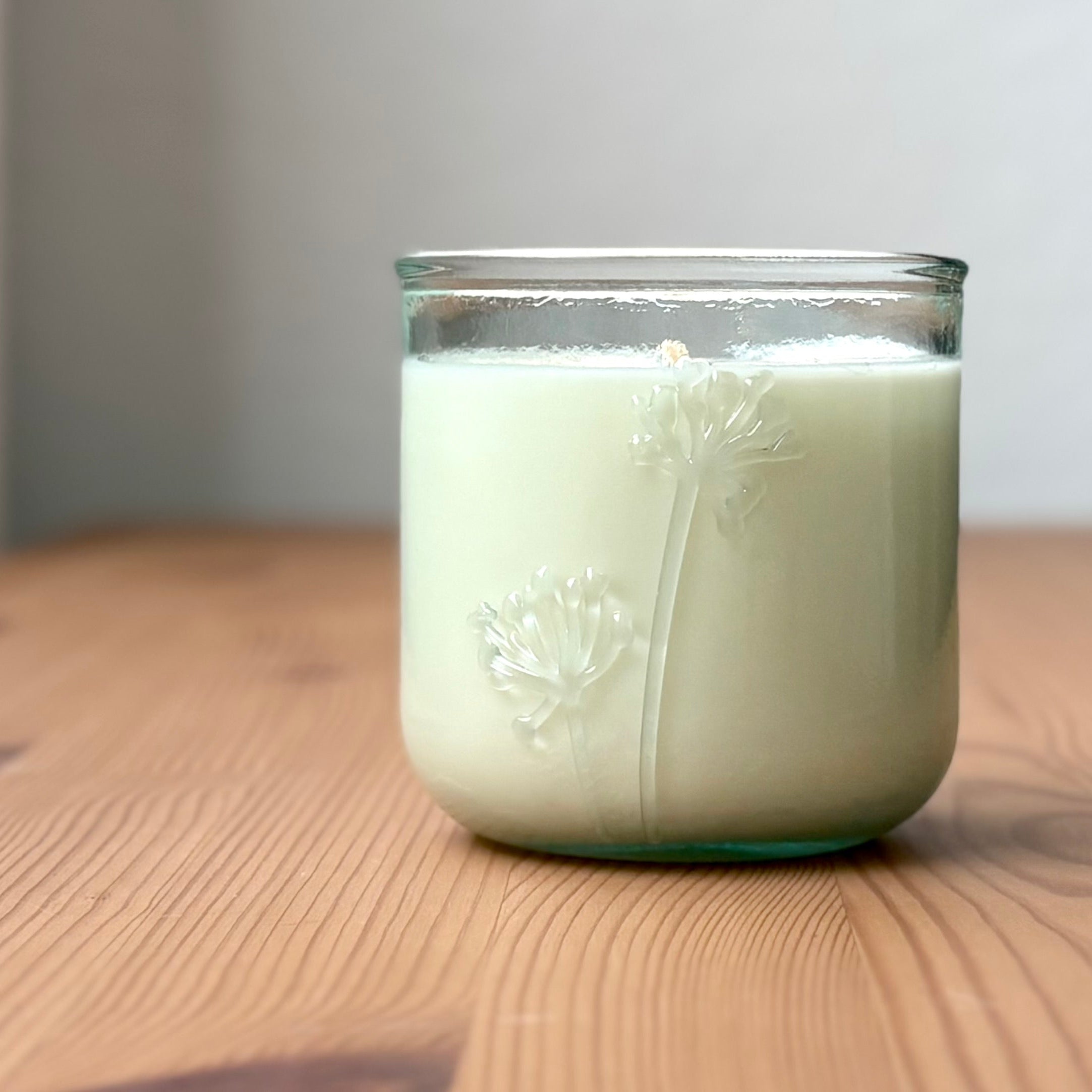 Organic candle in a recycled glass floral jar on a wooden surface
