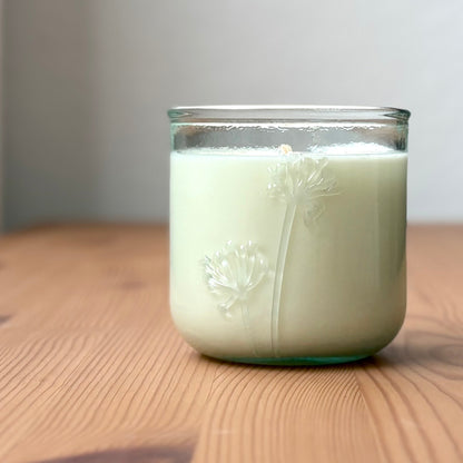 Organic candle in a recycled glass floral jar on a wooden surface