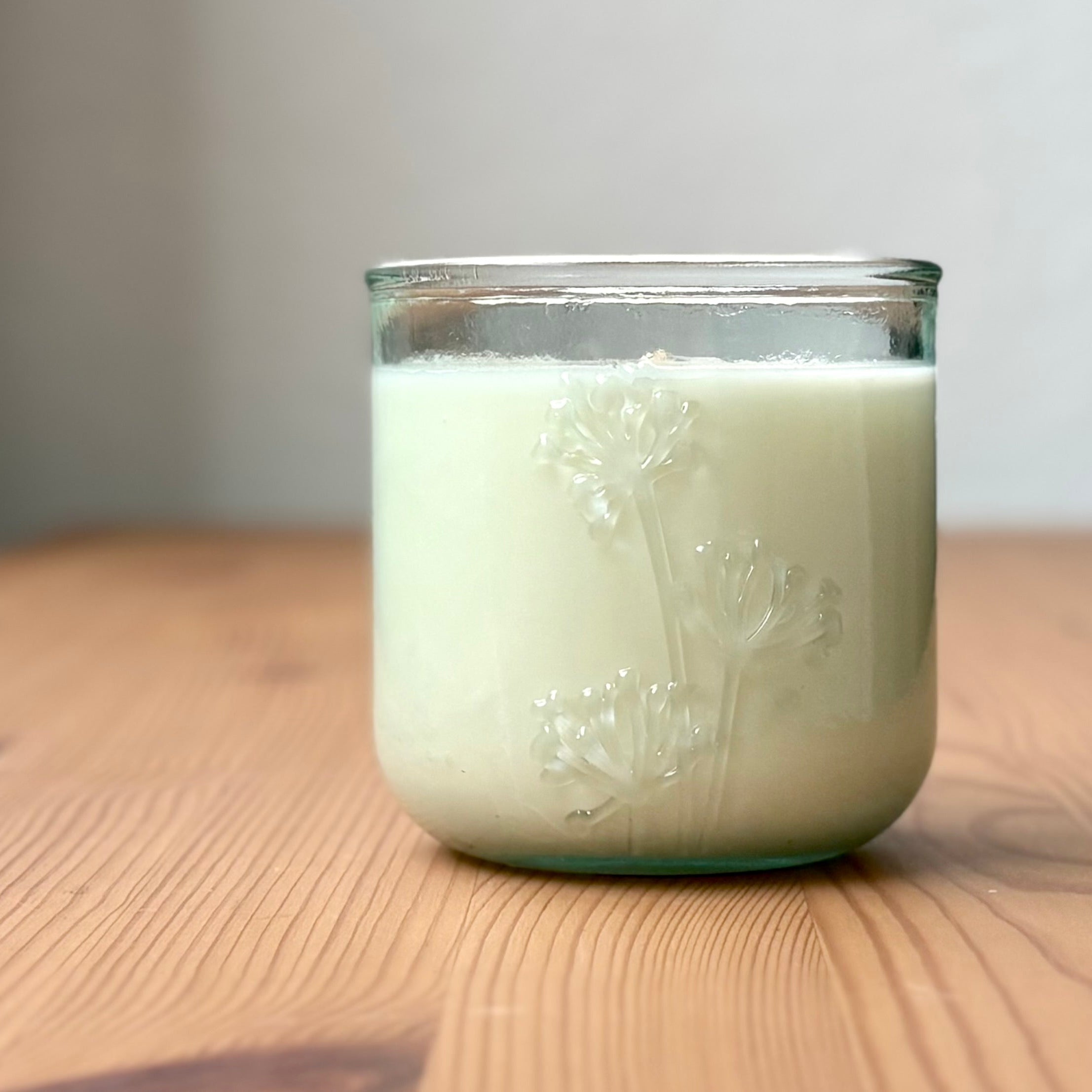 Organic candle in a recycled glass floral jar on a wooden surface