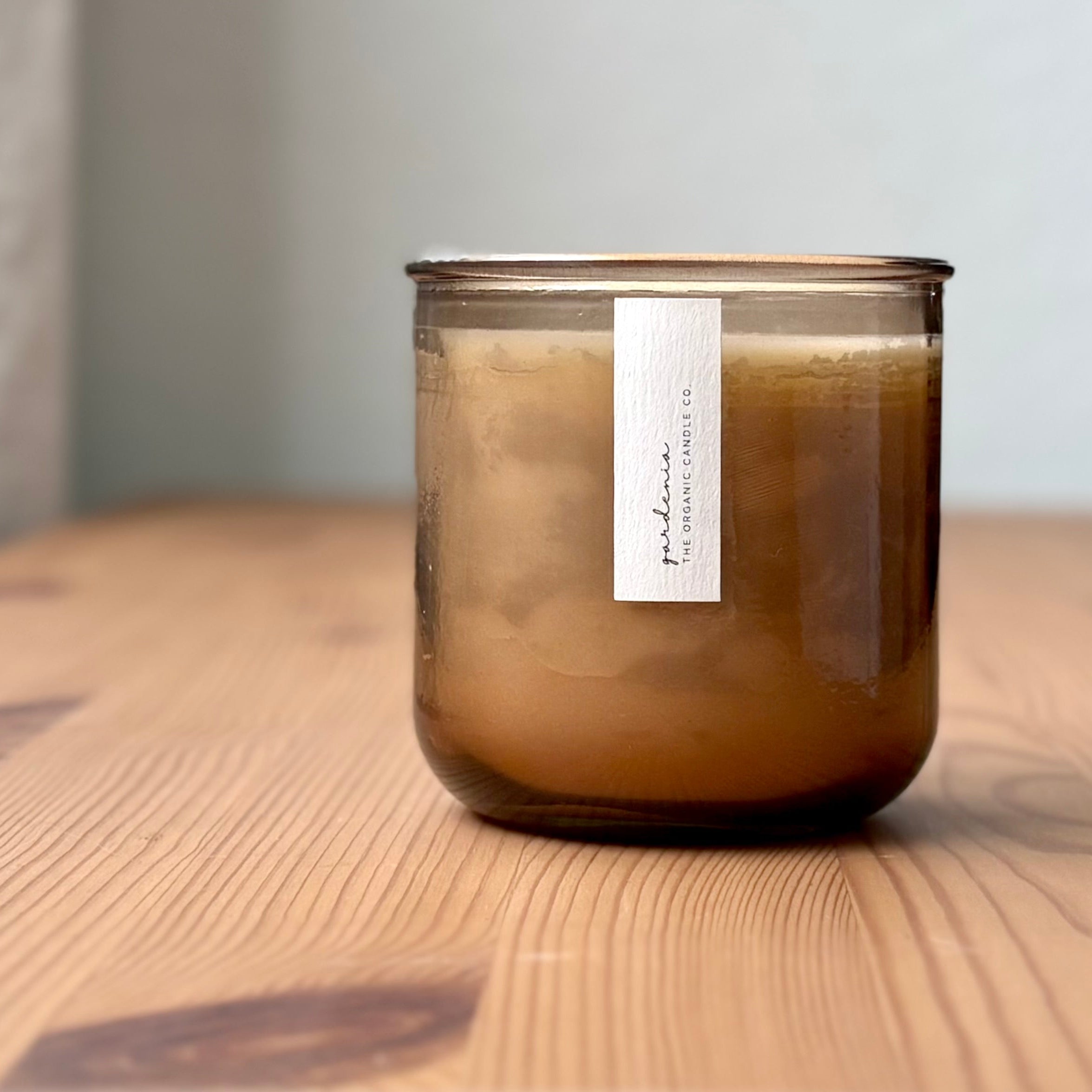 Organic candle in rose recycled glass jar on a wooden background. A label reads "gardenia; The Organic Candle Co."