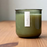 Organic candle in green recycled glass jar on a wooden background. A label reads "lavender; The Organic Candle Co."