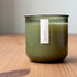 Organic candle in green recycled glass jar on a wooden background. A label reads "lavender; The Organic Candle Co."