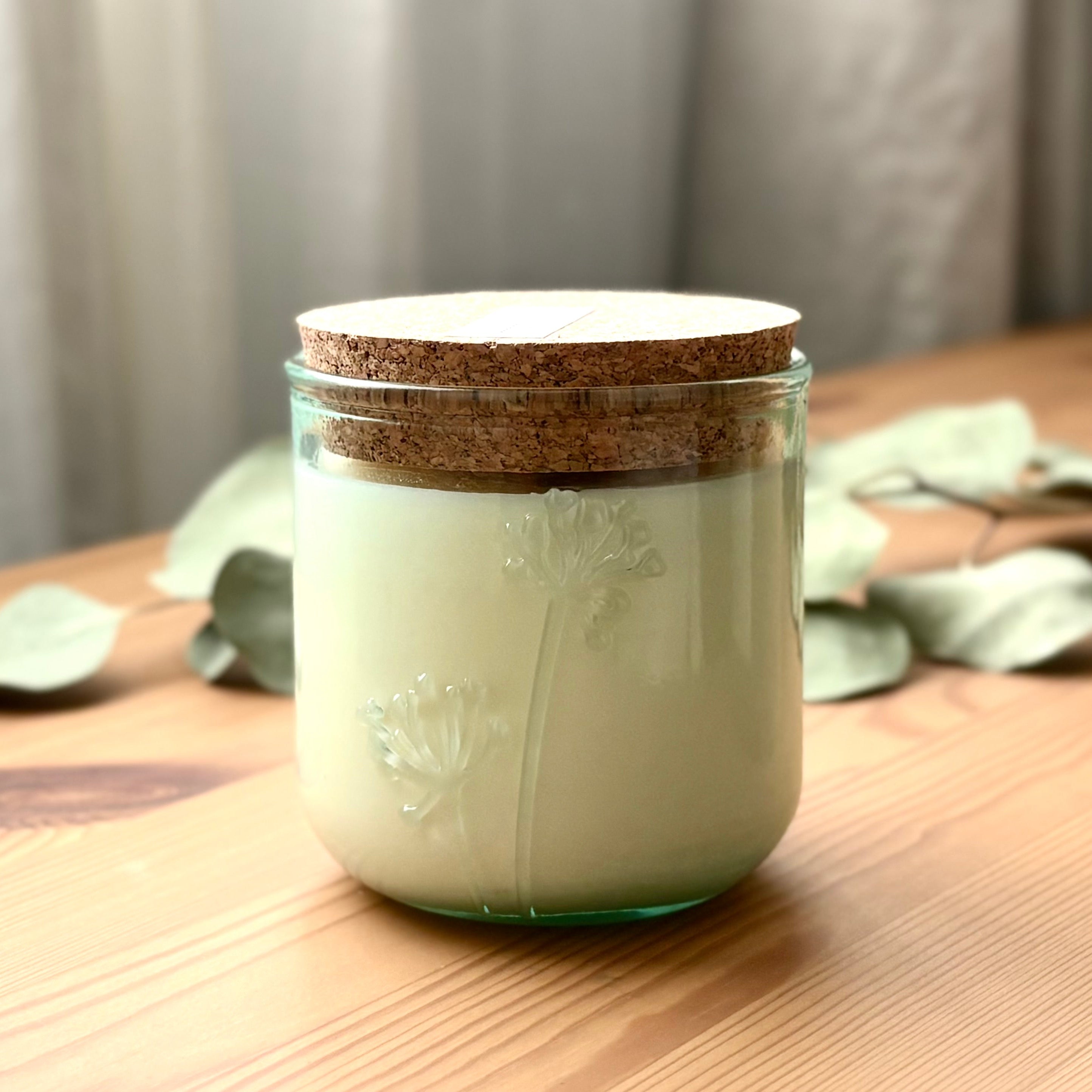 Organic candle in a recycled glass floral jar with a cork on a wooden surface.