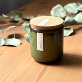 Organic candle in green recycled glass jar on a wooden background. A label reads "lavender; The Organic Candle Co."