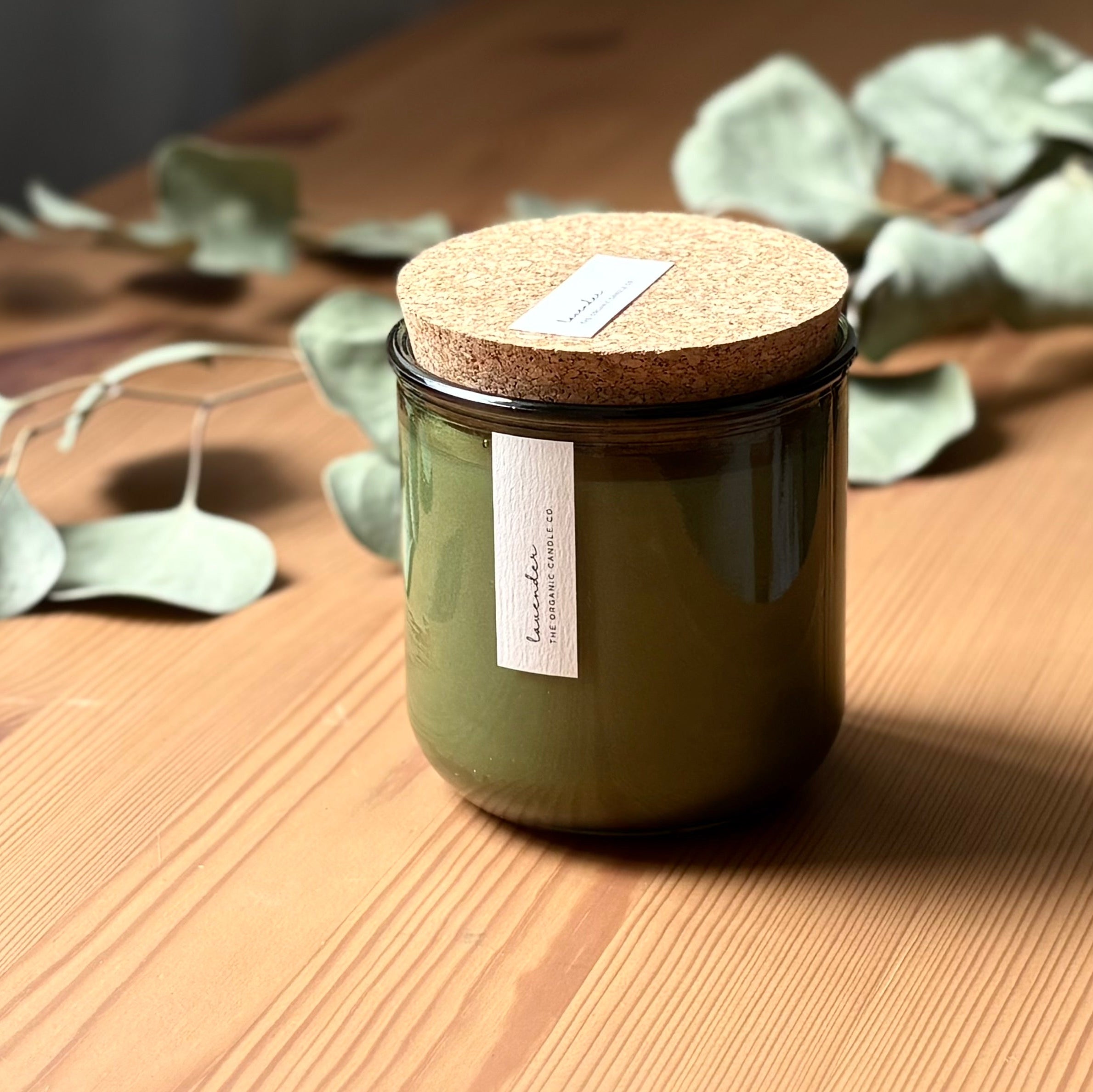 Organic candle in green recycled glass jar on a wooden background. A label reads "lavender; The Organic Candle Co."