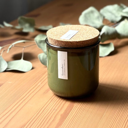Organic candle in green recycled glass jar on a wooden background. A label reads "lavender; The Organic Candle Co."