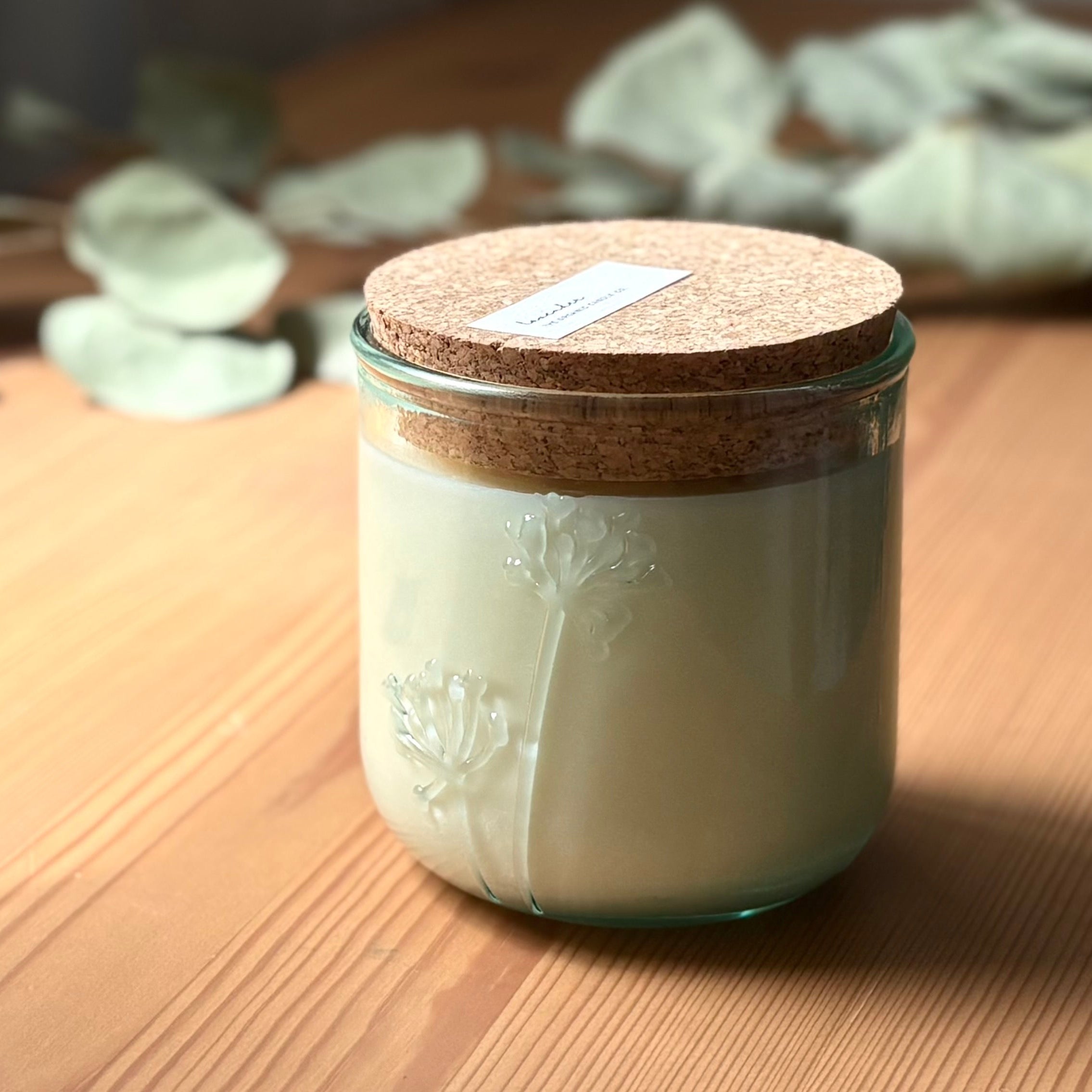 Organic candle in a recycled glass floral jar with a cork on a wooden surface.