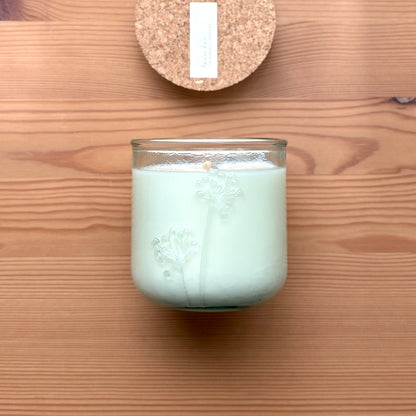 Organic candle in a recycled glass floral jar on a wooden surface