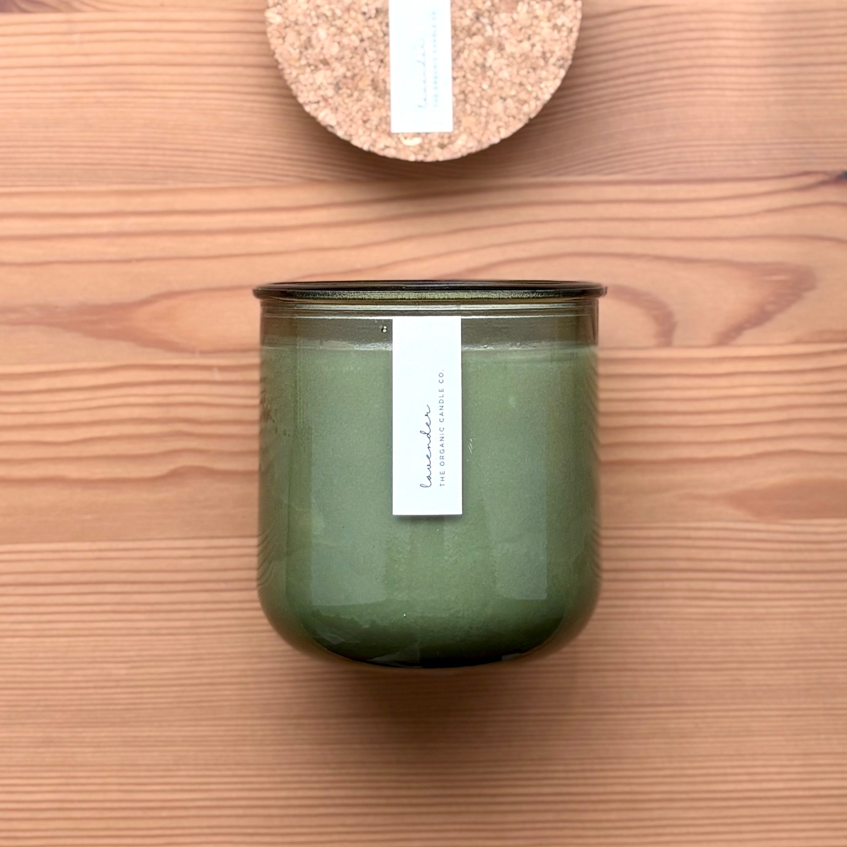 Organic candle in green recycled glass jar on a wooden background. A label reads "lavender; The Organic Candle Co."