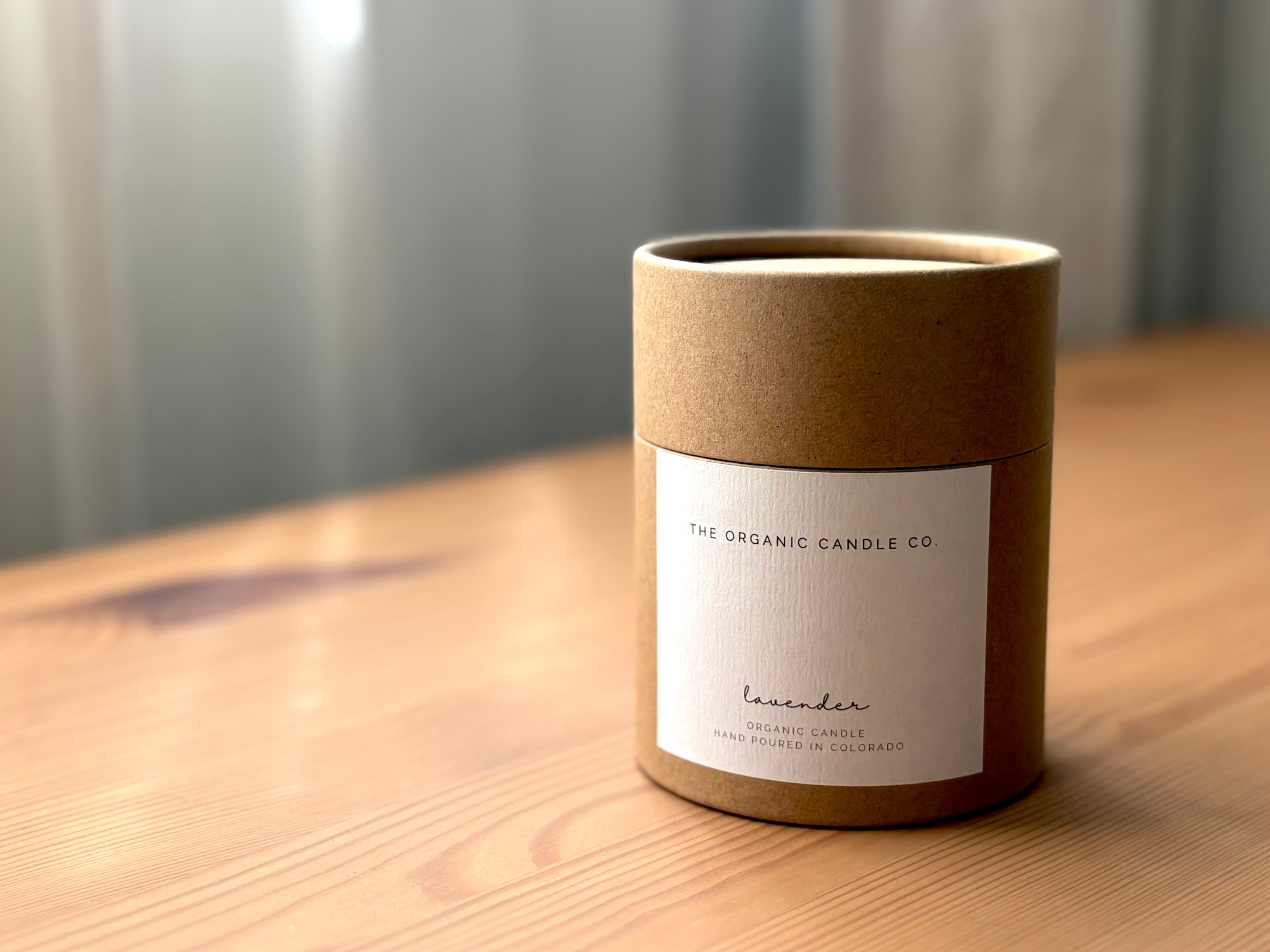 Organic candle in a kraft container with a "The Organic Candle Co." label on a wooden surface
