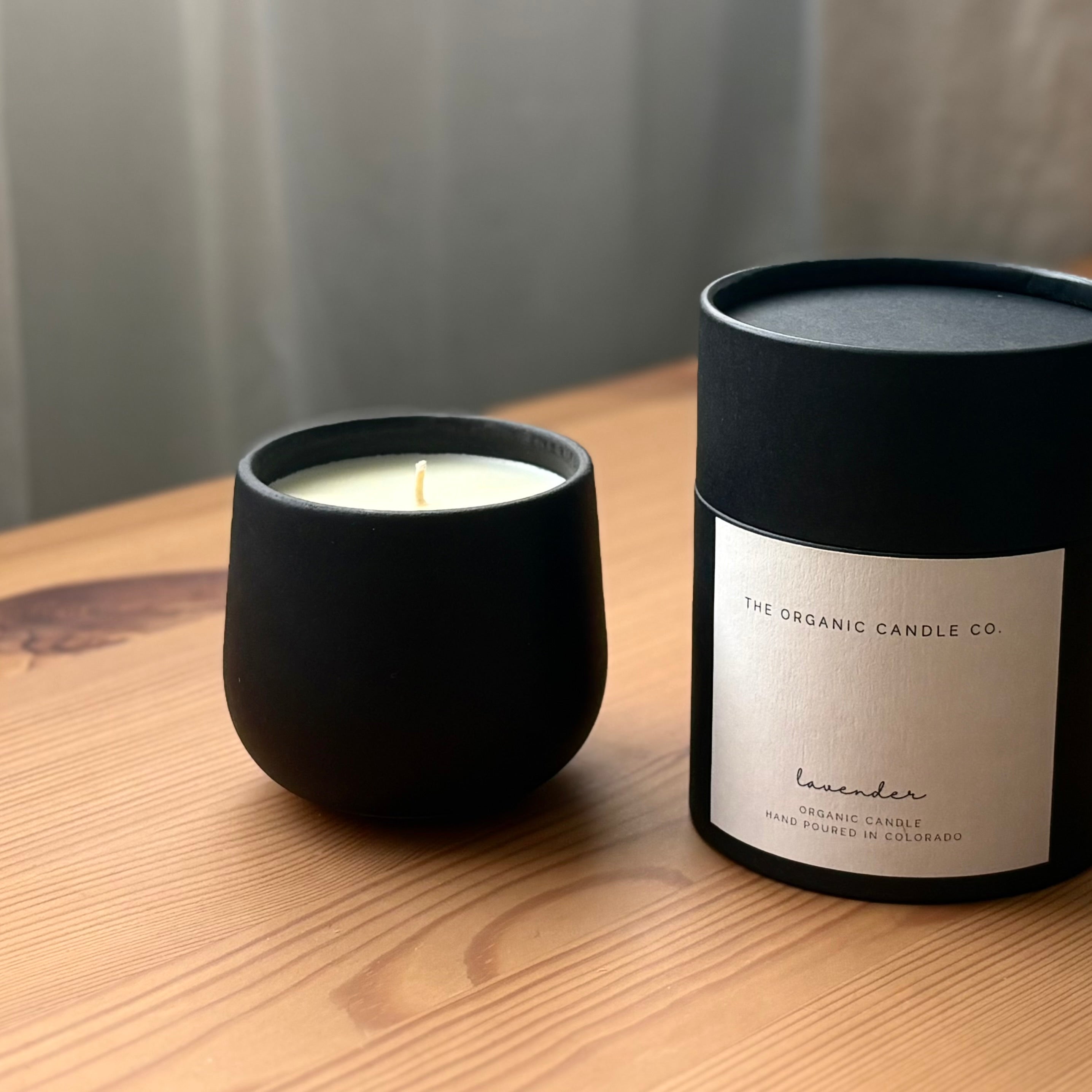 Black candle and packaging  that reads "The Organic Candle Co." on a wooden surface with a neutral background