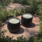 Two black ceramic organic candles on a stone path surrounded by green ground cover.