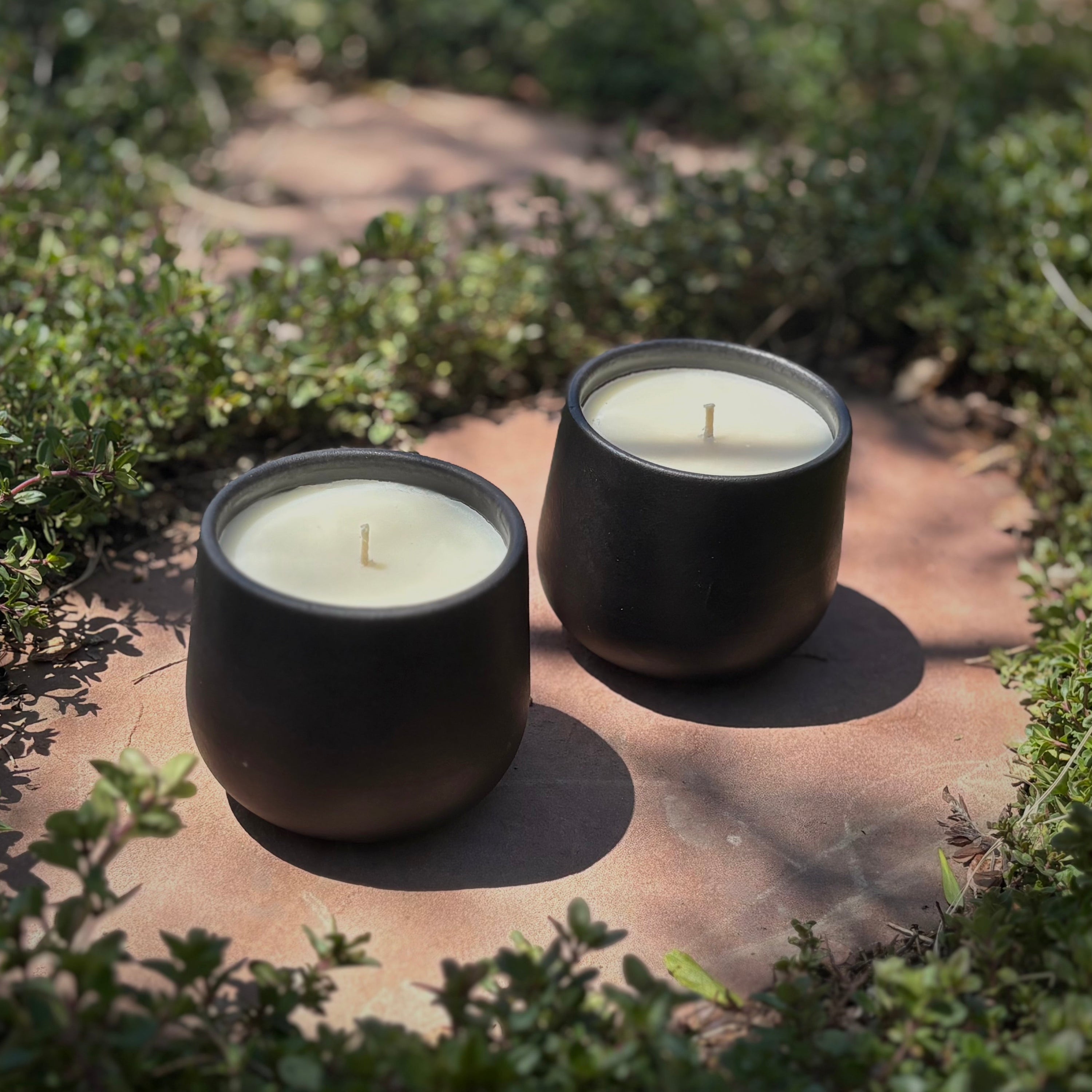 Two black ceramic organic candles on a stone path surrounded by green ground cover.