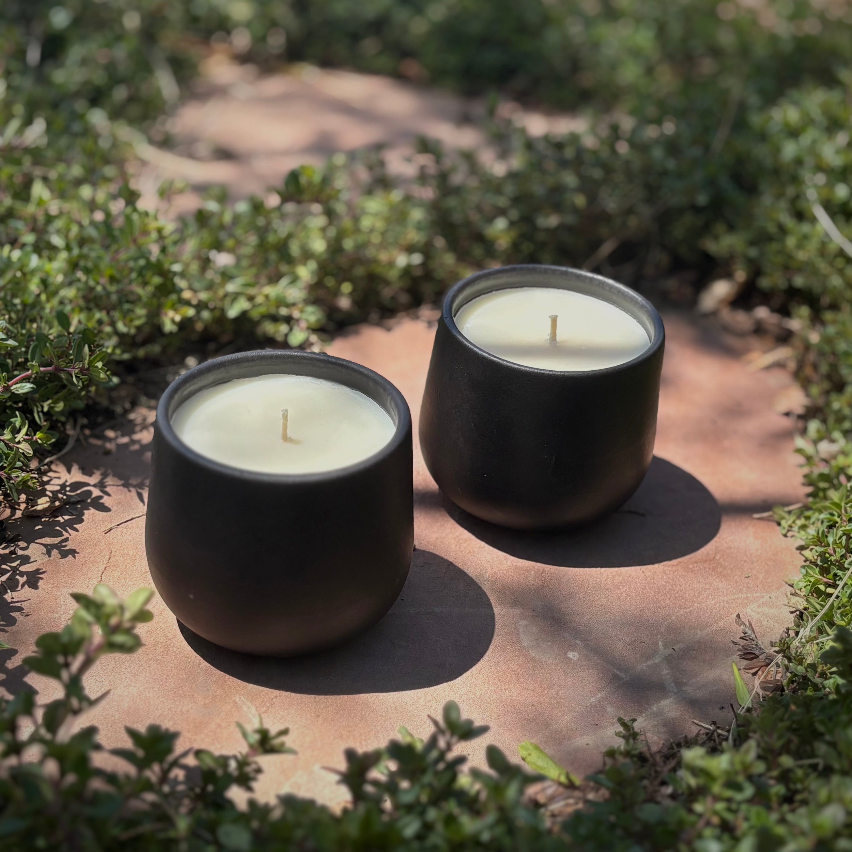 Two black ceramic organic candles on a stone path surrounded by green ground cover.