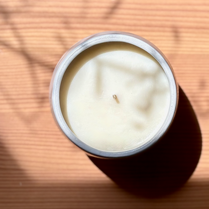 White ceramic organic candle on a wooden surface with shadows cast by leaves.
