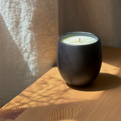 A matte black organic candle on a wooden surface, casting shadows.